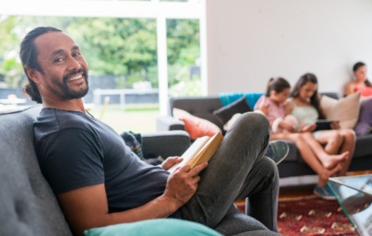 A man reads a book on the couch with his family