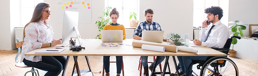 Four people work around a table on their laptops 