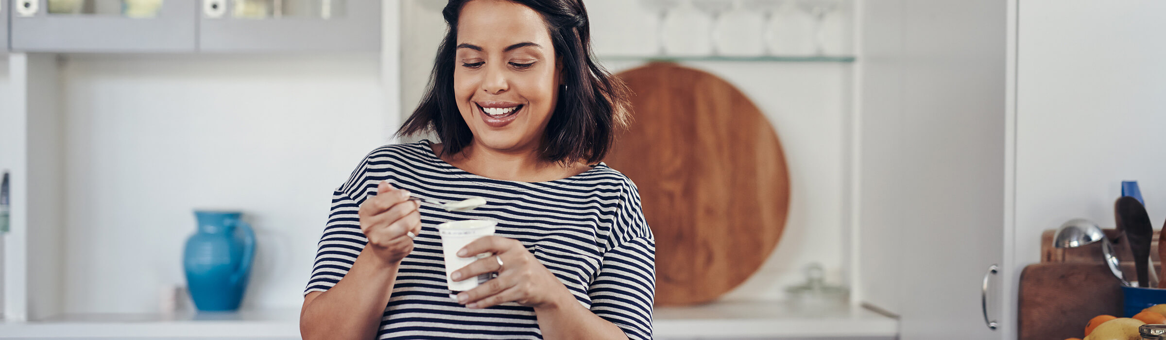 A woman smiles while eating a yoghurt