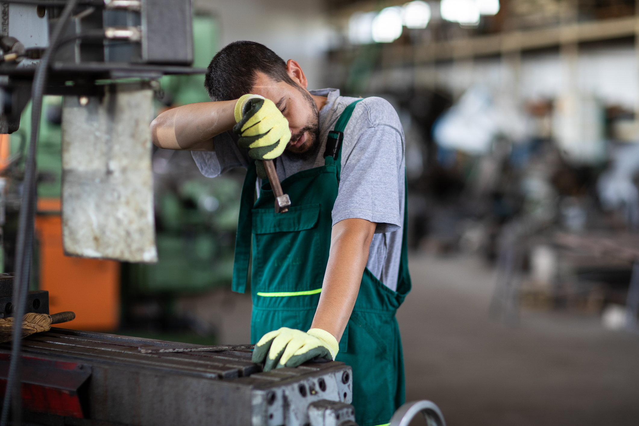 A man wipes his face while working at a machine