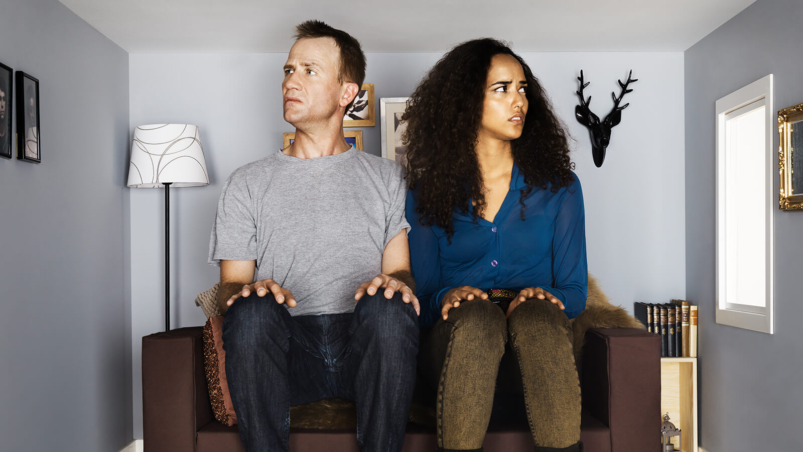 A man and woman sit together on a couch in a very small room