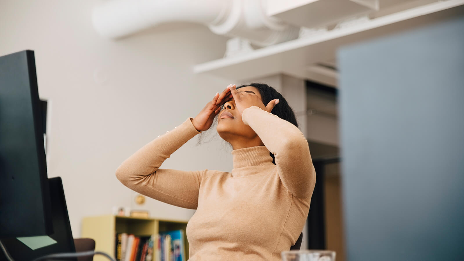 A woman rubs her eyes while working at her desk