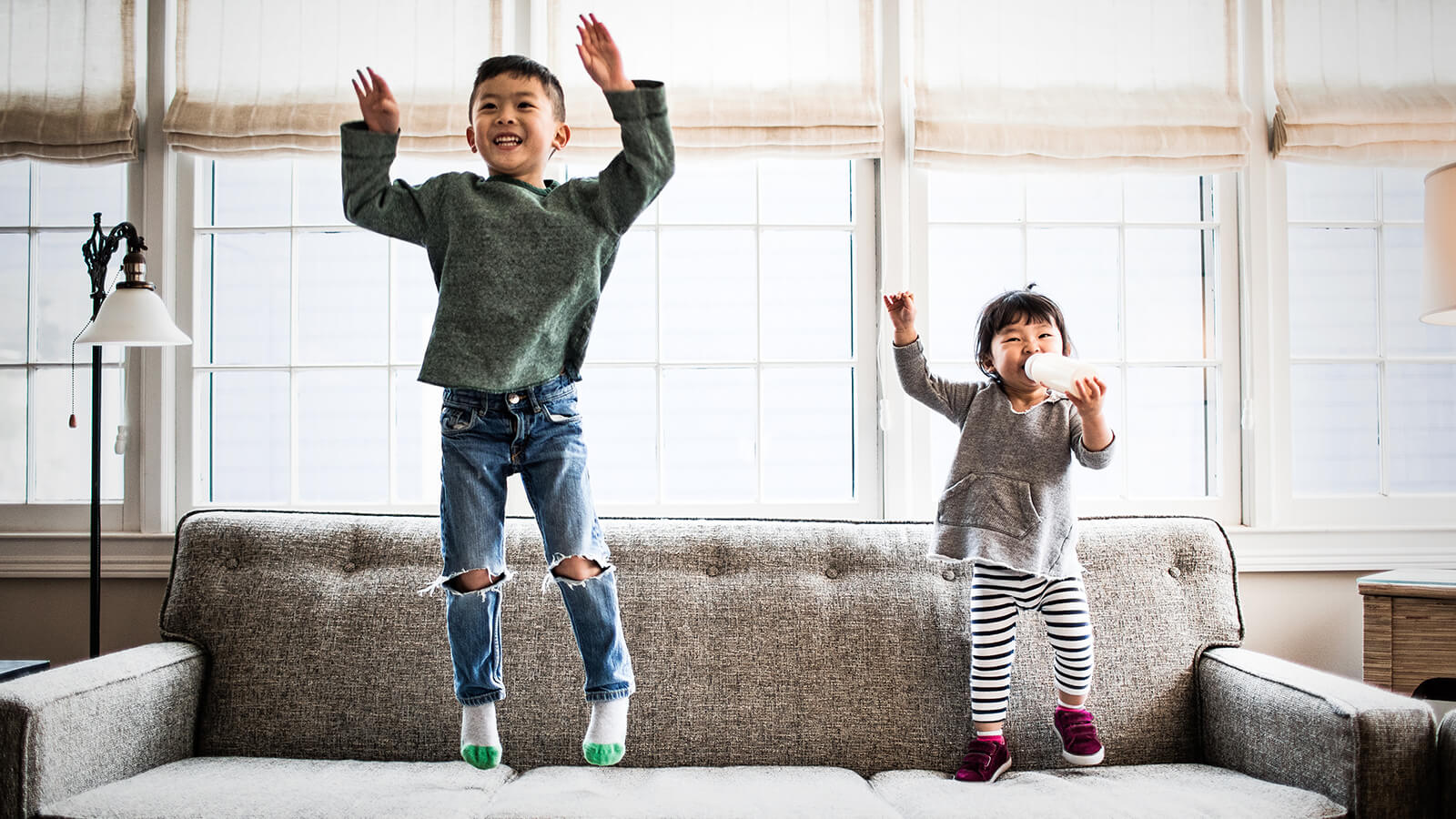 Two young kids jump on the sofa