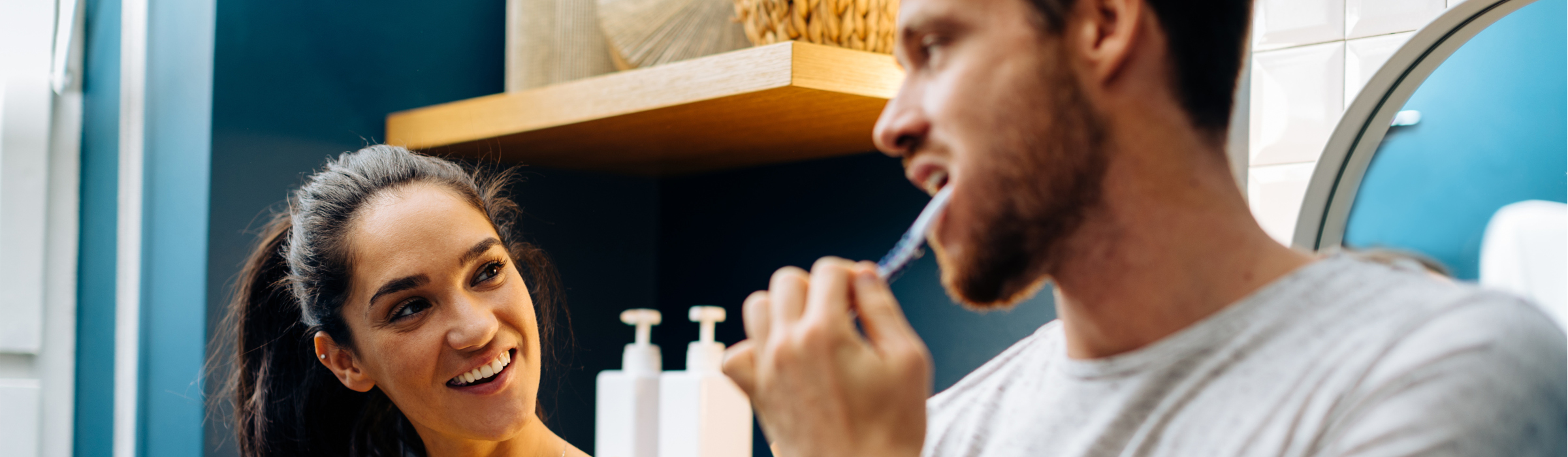 A man brushes his teeth while talking to a woman in the bathroom