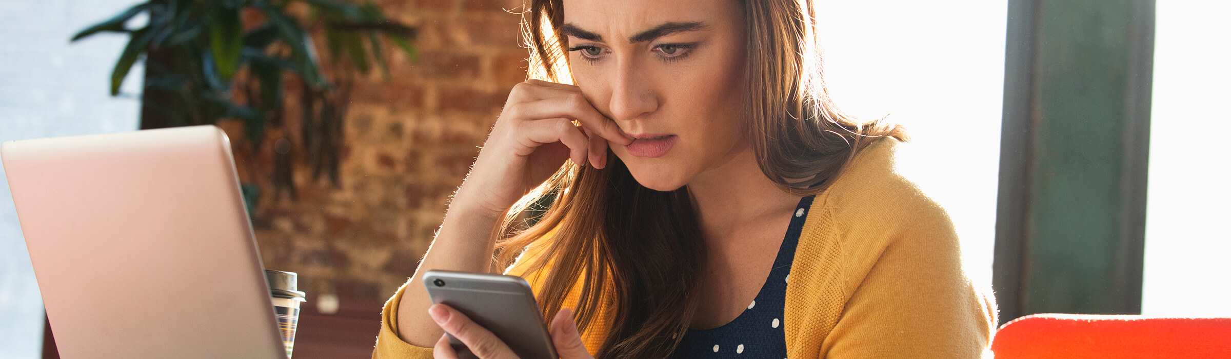 A woman anxiously looks at her phone while at her desk