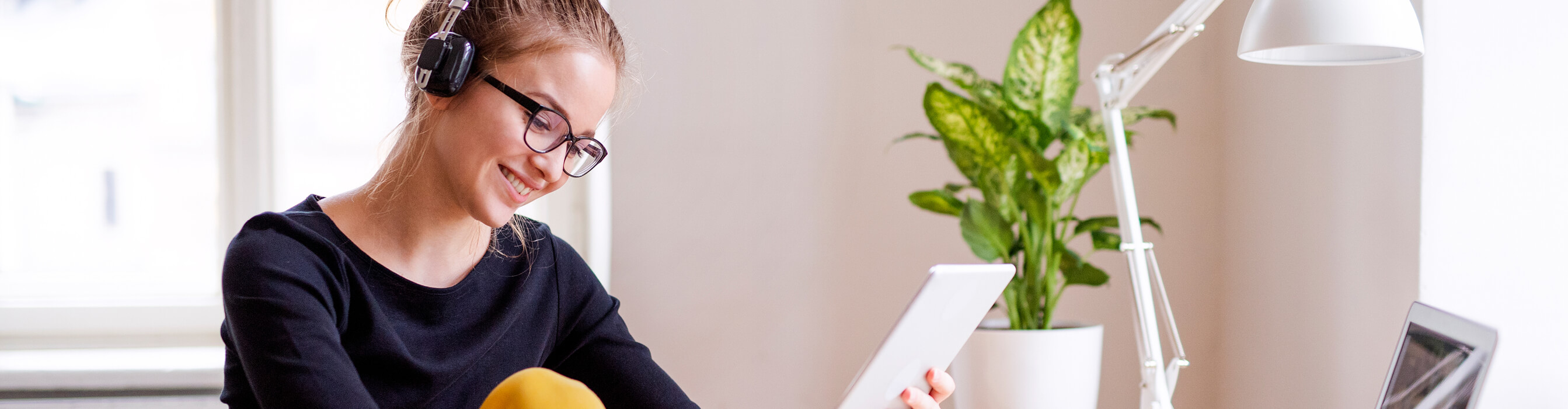 A woman with headphones on smiles while looking at her tablet computer