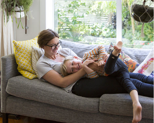 A mother and child laughing and hugging on their couch