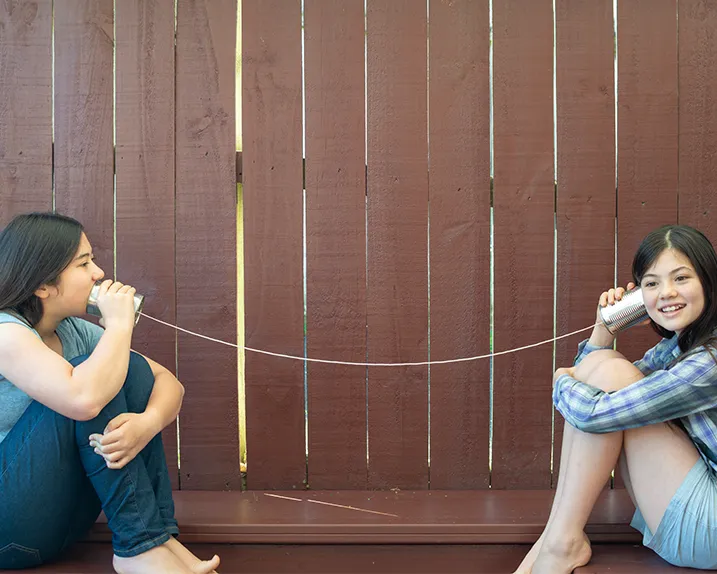 Two girls playing the telephone cup game