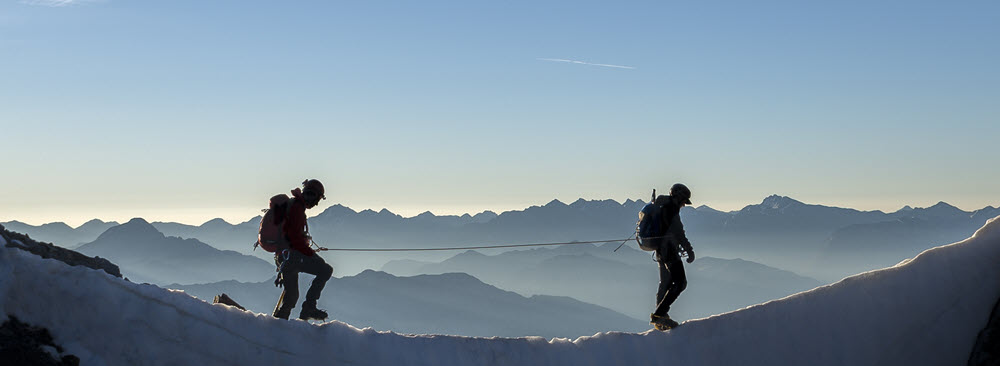 Two men walking on a mountain tethered by a security line