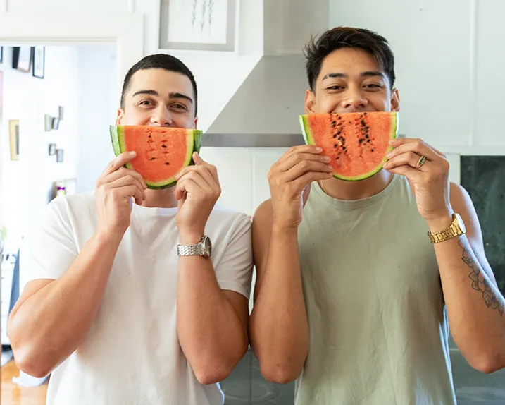 Two friends laughing, holding up watermelon slices